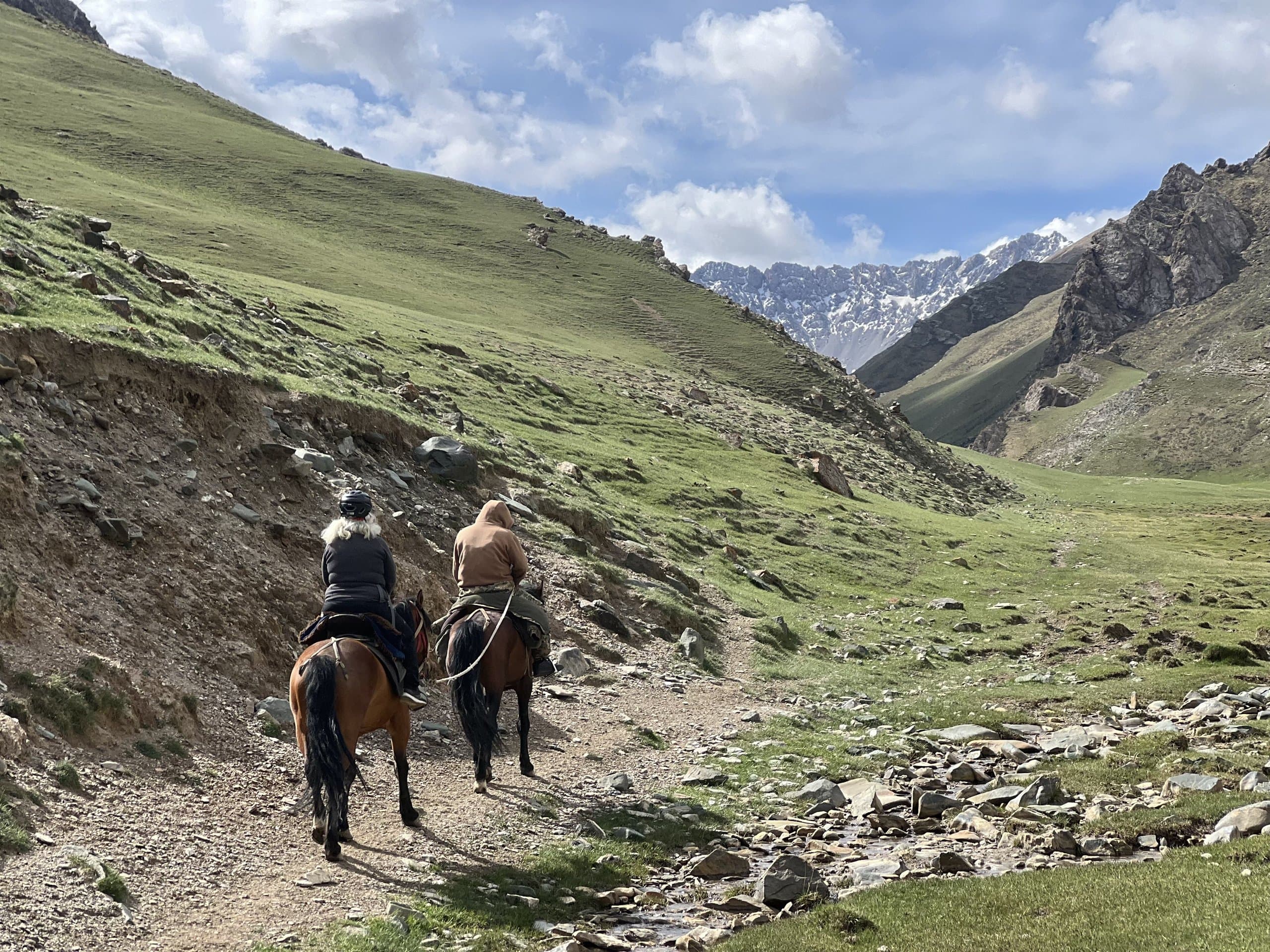 Two riders on horseback following a rocky trail through a mountain gorge