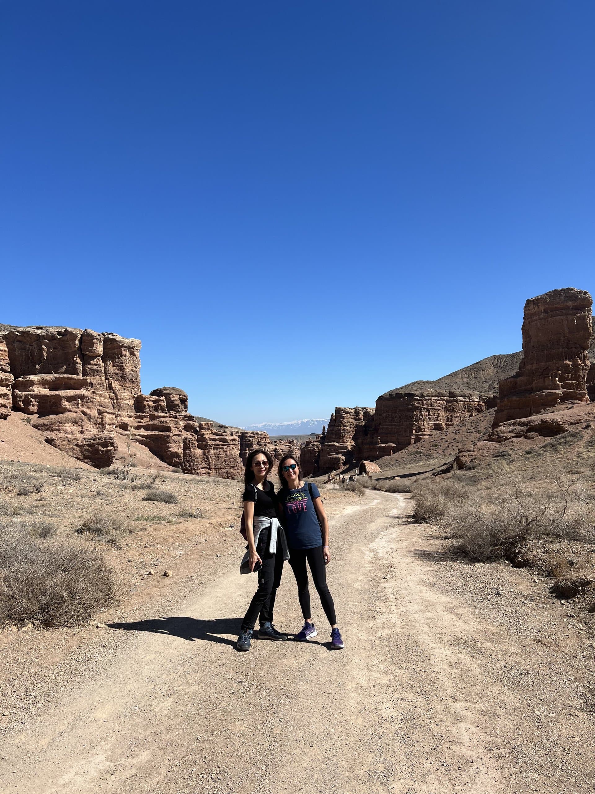 Travellers walking a sandy path between the tall rock towers of the Valley of Castles in Charyn Canyon